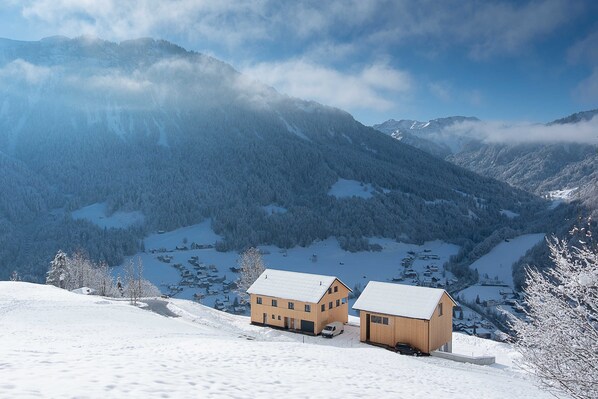 A snow-covered mountain landscape with two wooden buildings, one with a garage.
