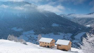 Un paysage montagneux enneigé avec deux bâtiments en bois, dont l’un est doté d’un garage.