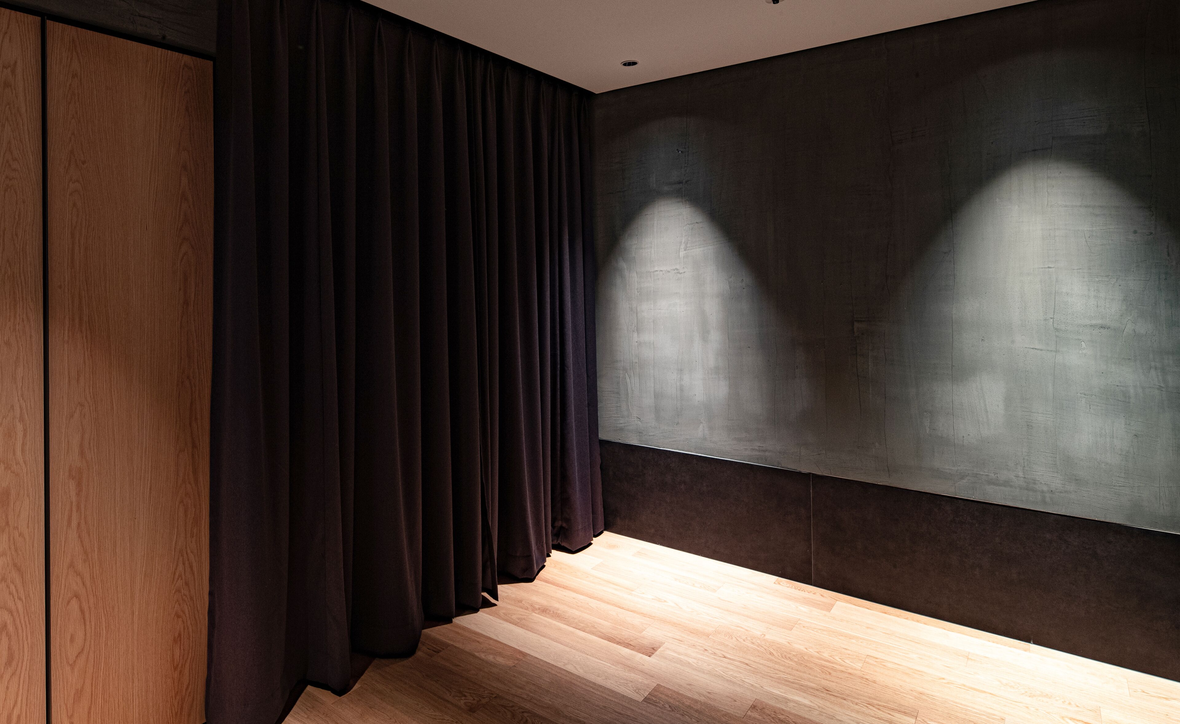 Una habitación con cortinas oscuras, un panel de pared de madera y una pared grande de textura oscura.