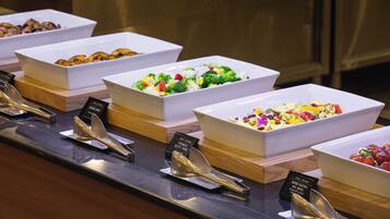 A buffet with various dishes in white bowls, arranged on a wooden counter with metal serving utensils.