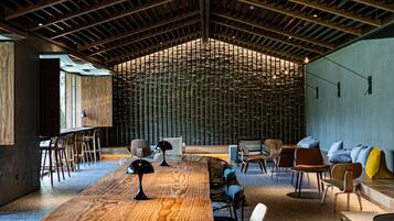 A spacious interior with a long wooden table, multiple chairs, and a high ceiling with exposed beams.