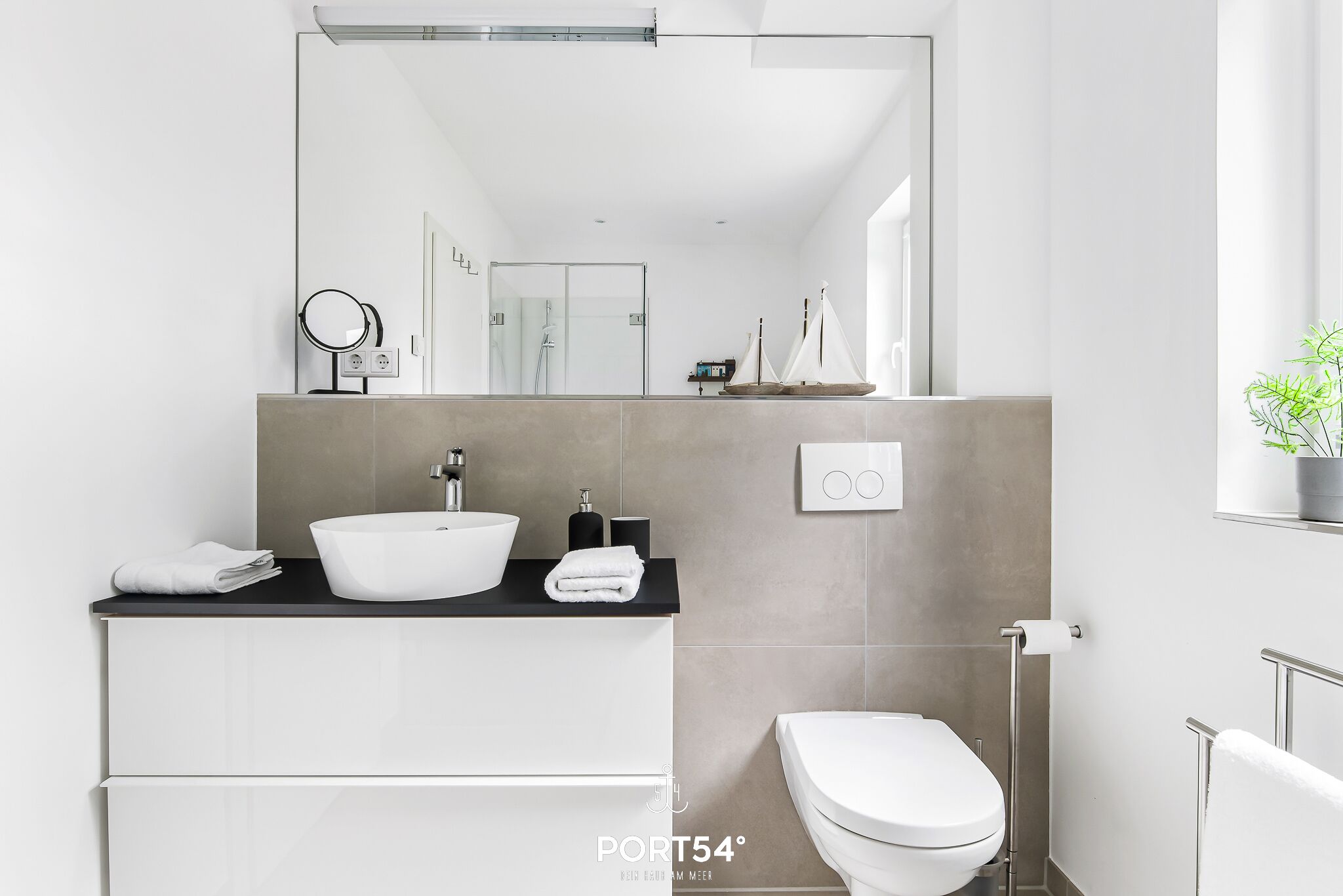 A modern bathroom with a white sink, a toilet, and a large mirror.