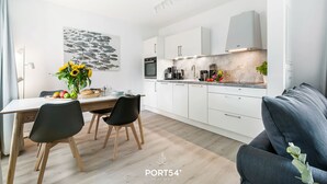 Una cucina moderna con mobili bianchi, forno integrato e macchina per il caffè. C'è un tavolo da pranzo con sedie e un vaso di fiori.