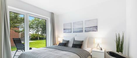 A modern bedroom with a large bed, a nightstand, a bedside table, and a view of the outdoors.