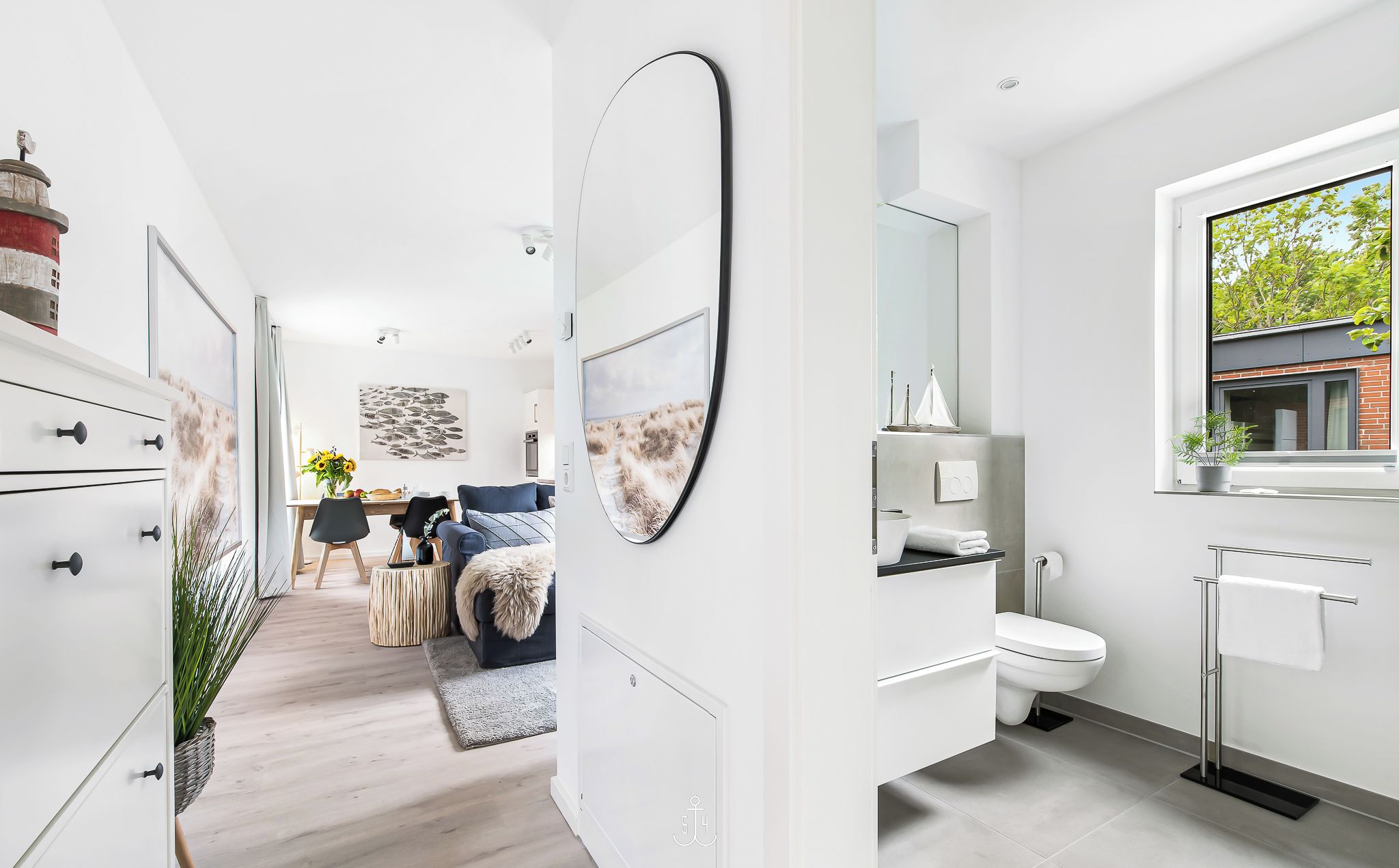 A modern, minimalist bathroom with a large mirror, a toilet, and a window providing natural light.