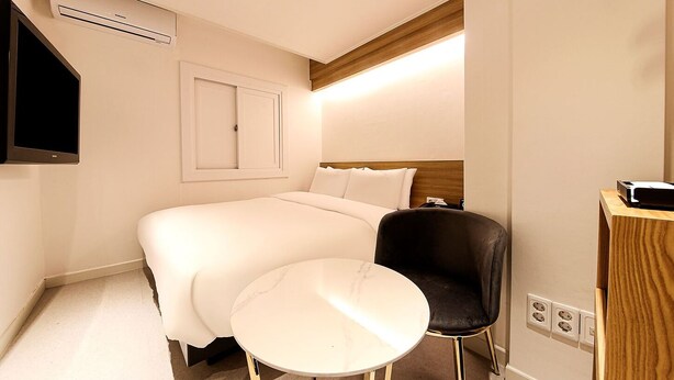 A hotel room with a bed, a chair, a small table, a TV, and a wooden headboard. - Busan Seomyeon Business Hotel J7 (Busan)