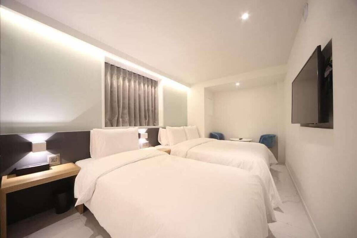 Ein Hotelzimmer mit zwei Betten, einem Schreibtisch, einem Stuhl, einem Fernseher und einem Fenster mit Vorhängen.