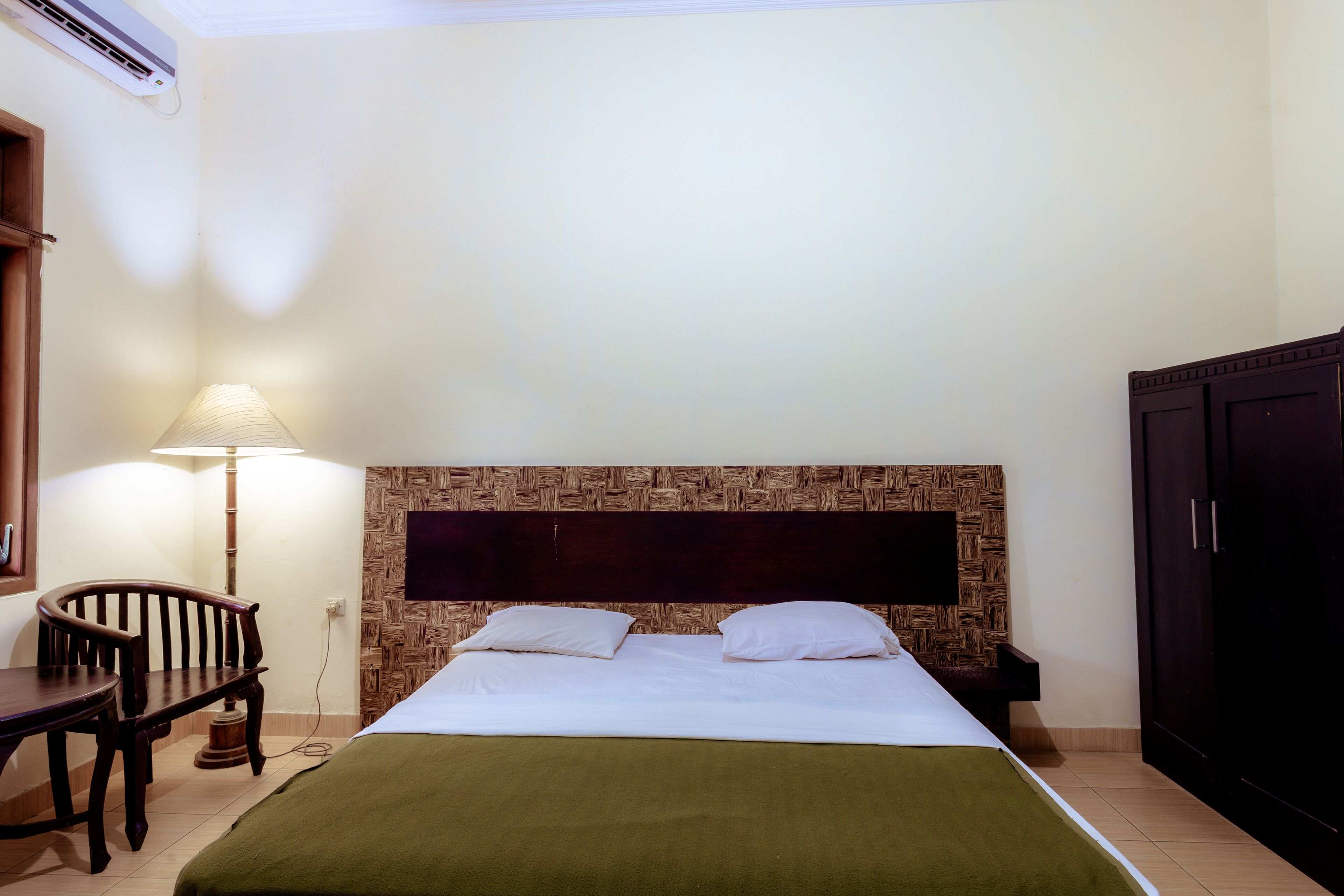 A hotel room with a bed, a desk, a chair, a lamp, and a wardrobe.