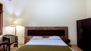 A hotel room with a bed, a desk, a chair, a lamp, and a wardrobe.