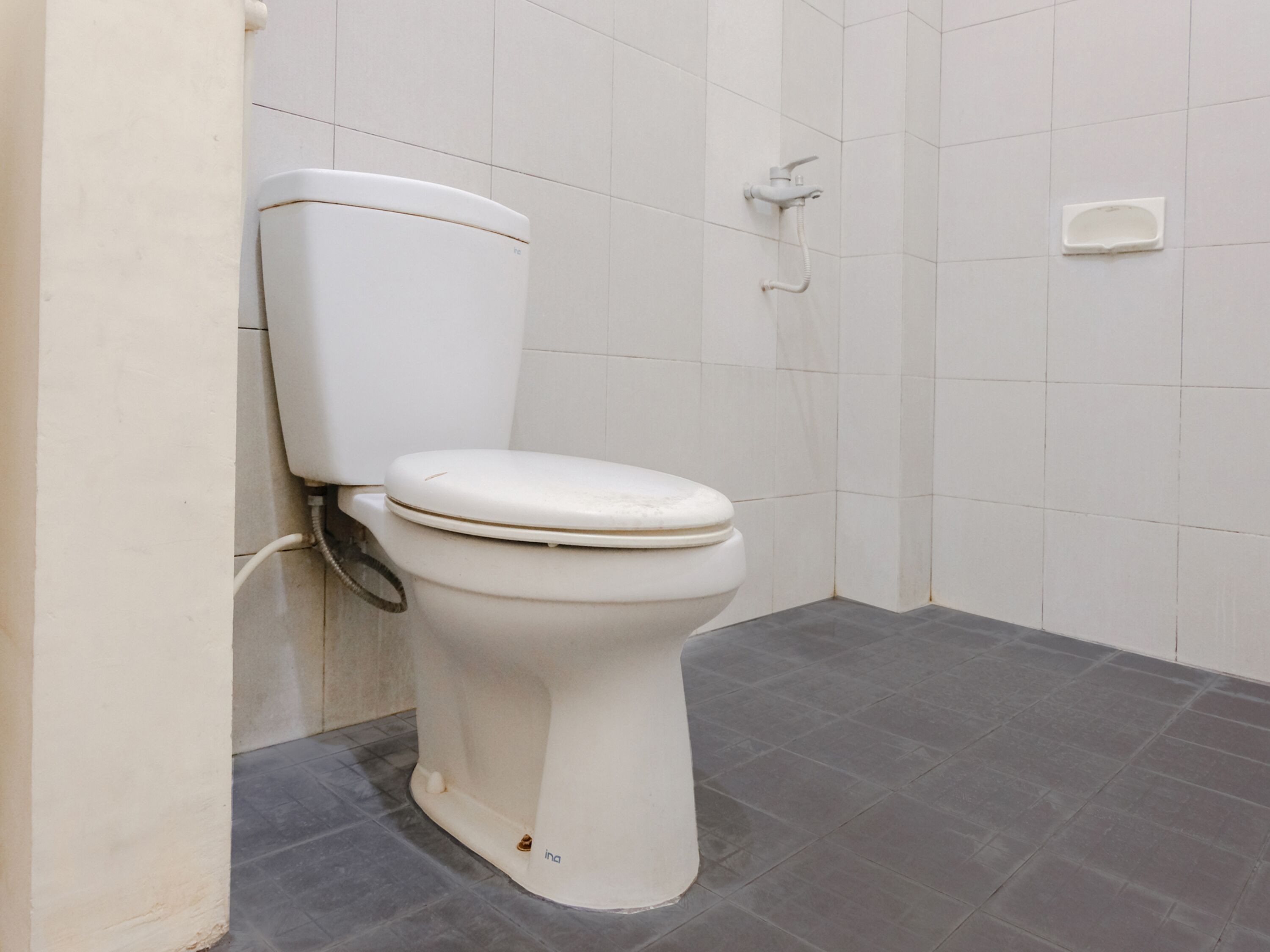 Eine weiße Toilette in einem Badezimmer mit grauen Fliesen an Boden und Wänden.