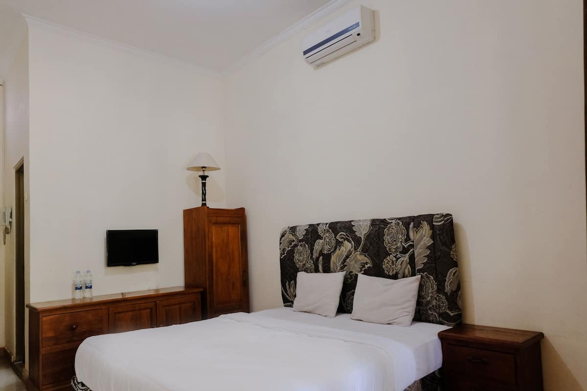 Een slaapkamer met een bed, nachtkastje, lamp, televisie en airconditioning.