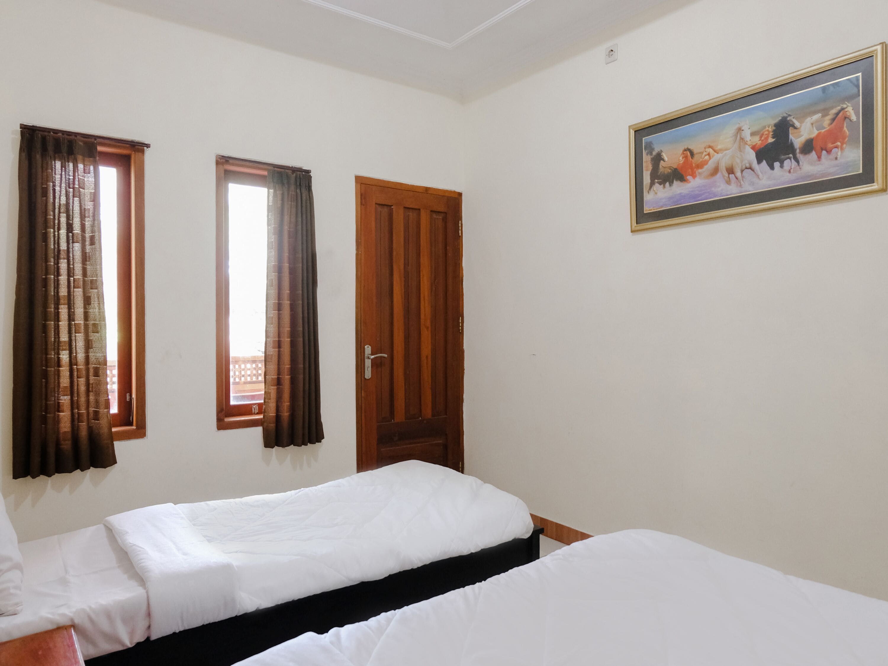 Une chambre avec deux lits, une porte en bois et un tableau au mur.