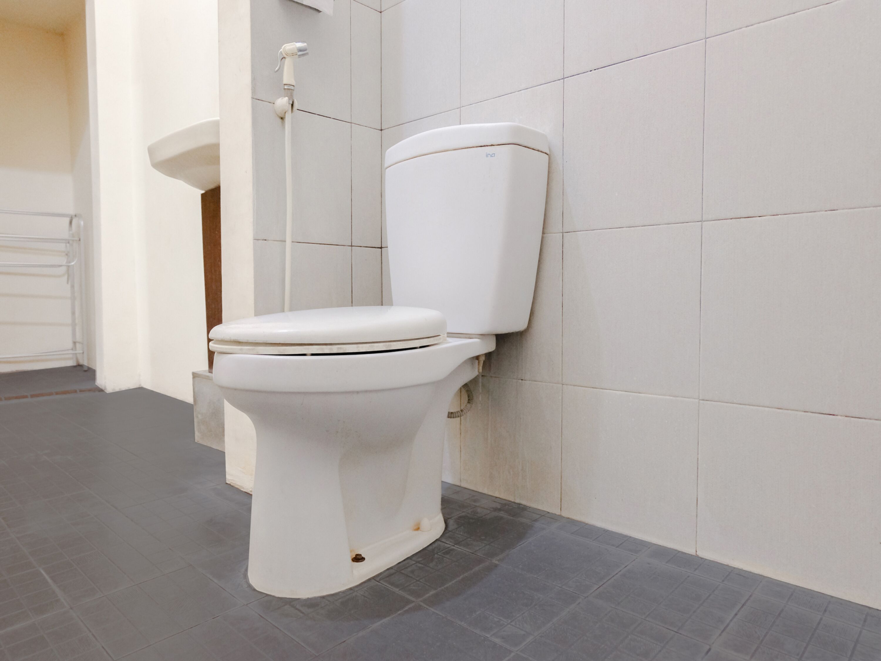 A white toilet with a tank and seat, a showerhead, and a tiled floor.