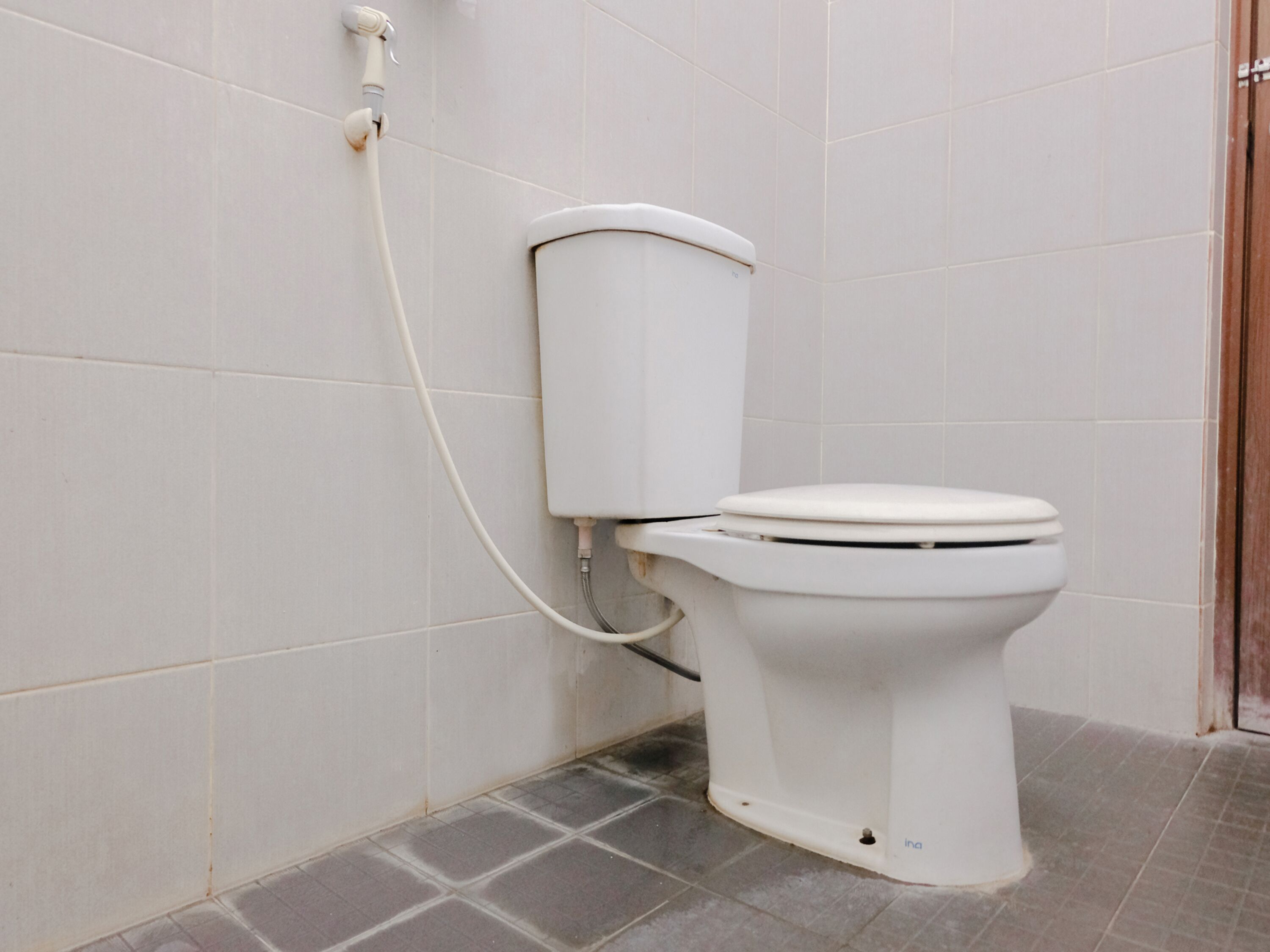 Inodoro blanco con tanque y asiento, conectado a un mecanismo de descarga en la pared.
