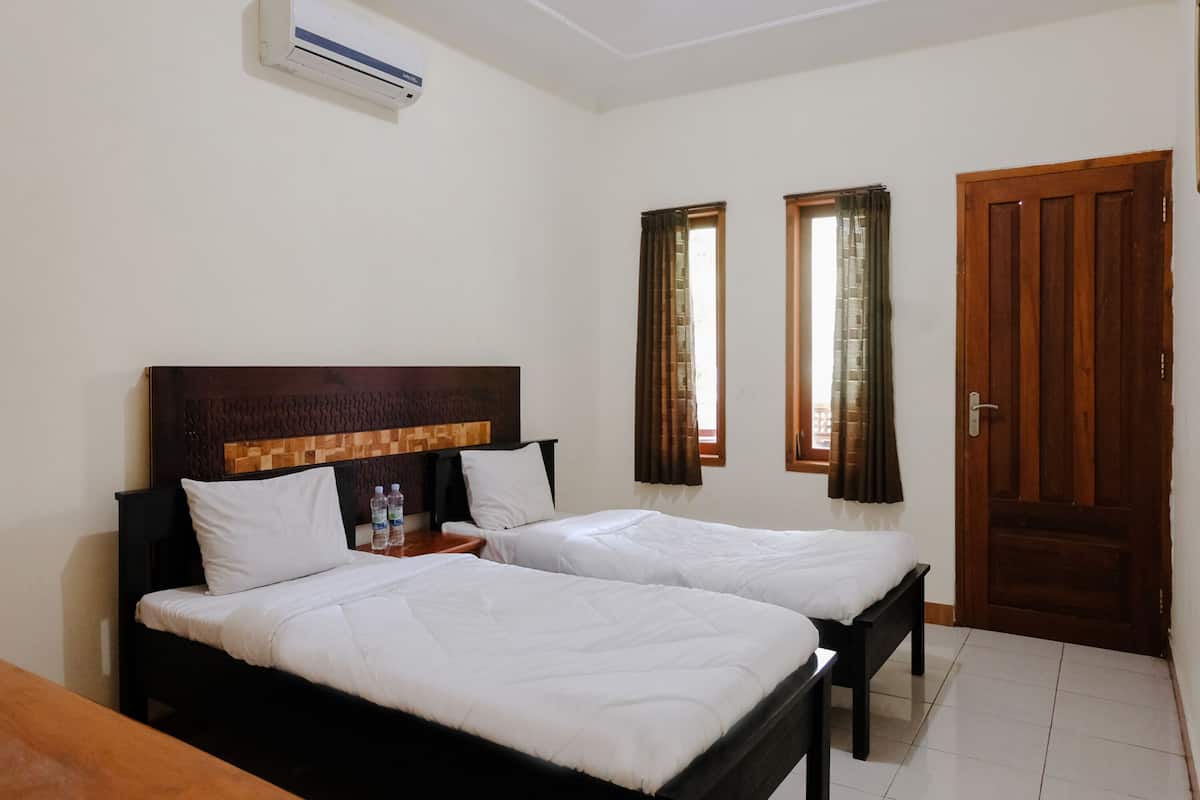 Een hotelkamer met twee bedden, een houten hoofdbord, een houten deur en een airconditioner.