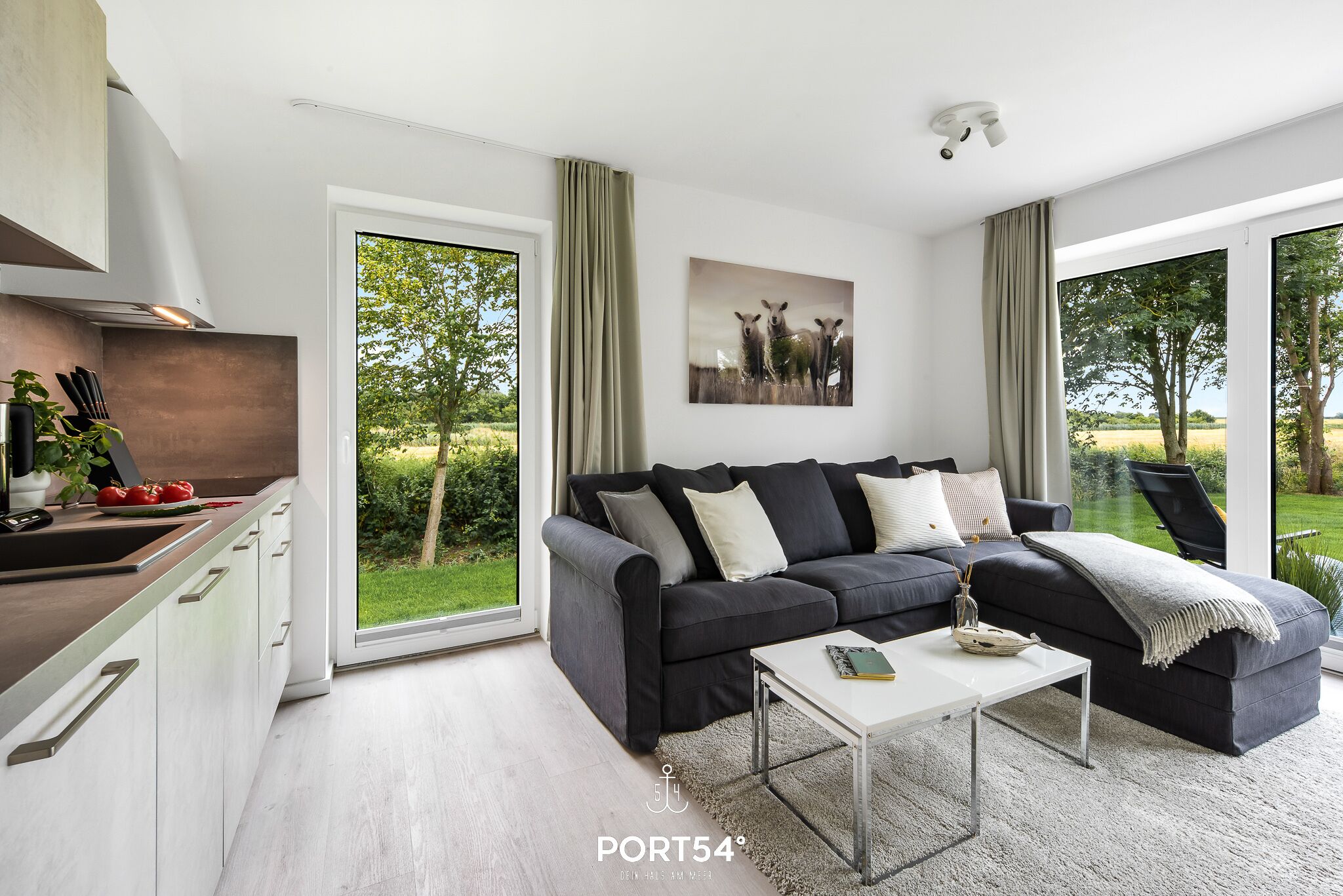 Una sala de estar moderna con un sofá gris oscuro, una mesa de centro blanca y un ventanal con vistas a zonas verdes.