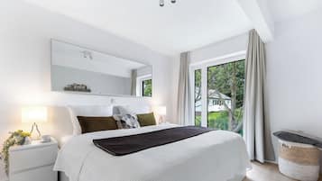 Un dormitorio moderno con una cama grande, una mesita de noche con lámpara, un espejo y vistas a zonas verdes.