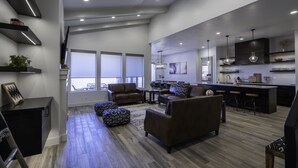 A modern living room with a sofa, ottoman, and coffee table, a dining area with chairs, and a kitchen with bar stools. - Arcadia 54 | Private Hot Tub * Ping Pong * Nintendo (Santa Clara)