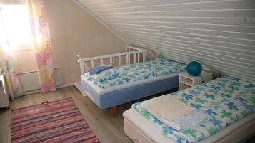 A small, cozy bedroom with two single beds, a colorful striped rug, and a window with patterned curtains.