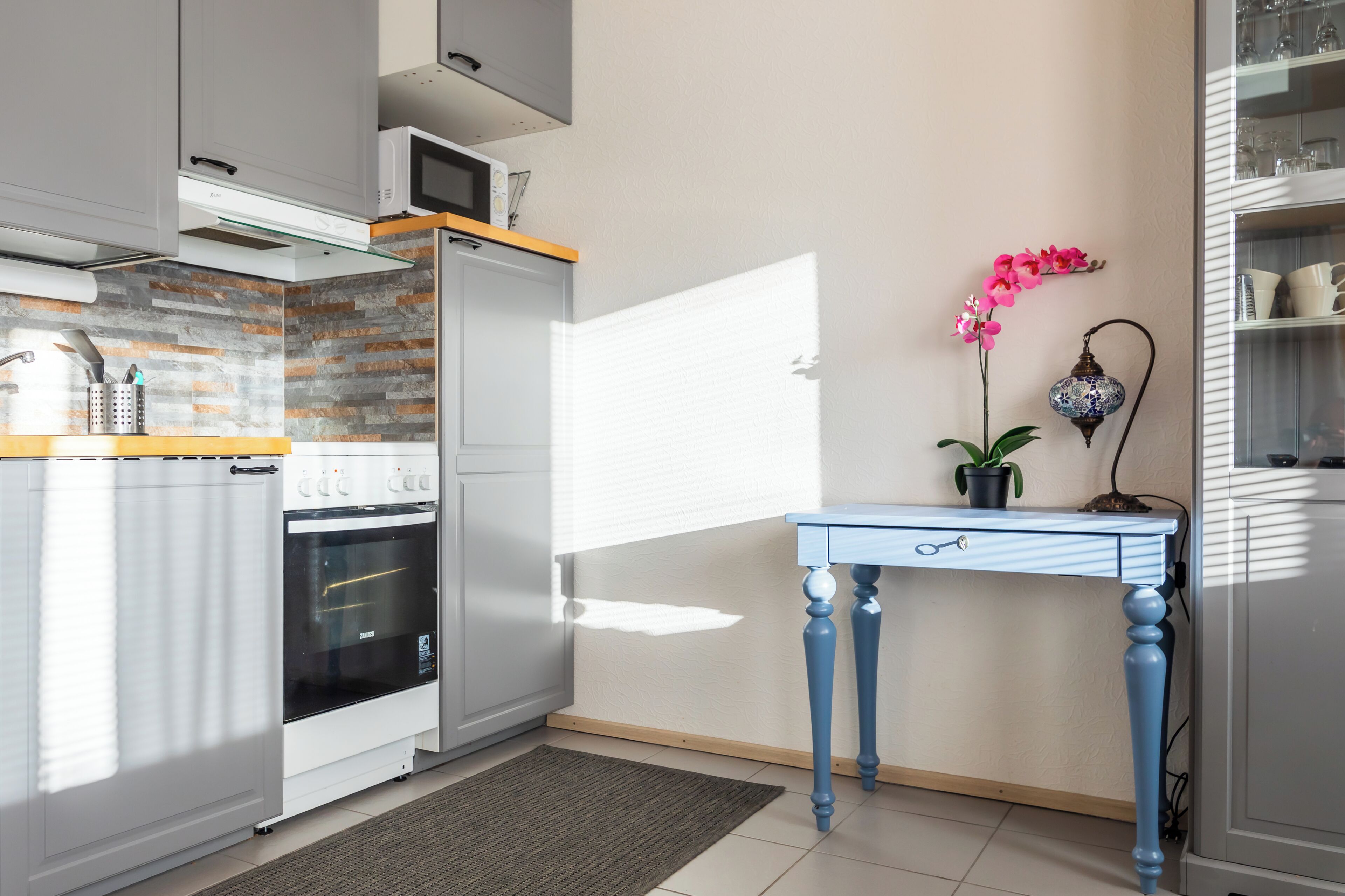 Una cocina con horno integrado, microondas y una mesa azul con una planta en maceta.