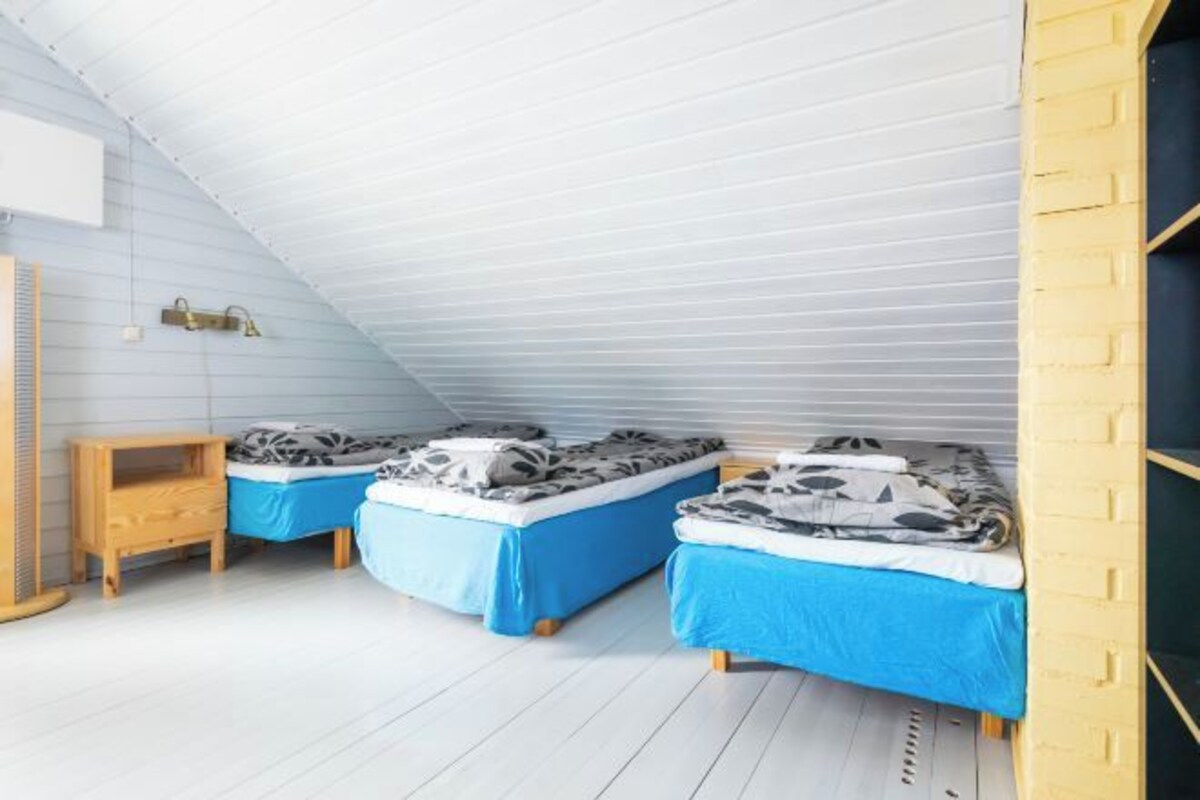 A room with two beds, each with blue bedding, a wooden nightstand, and a sloped ceiling.