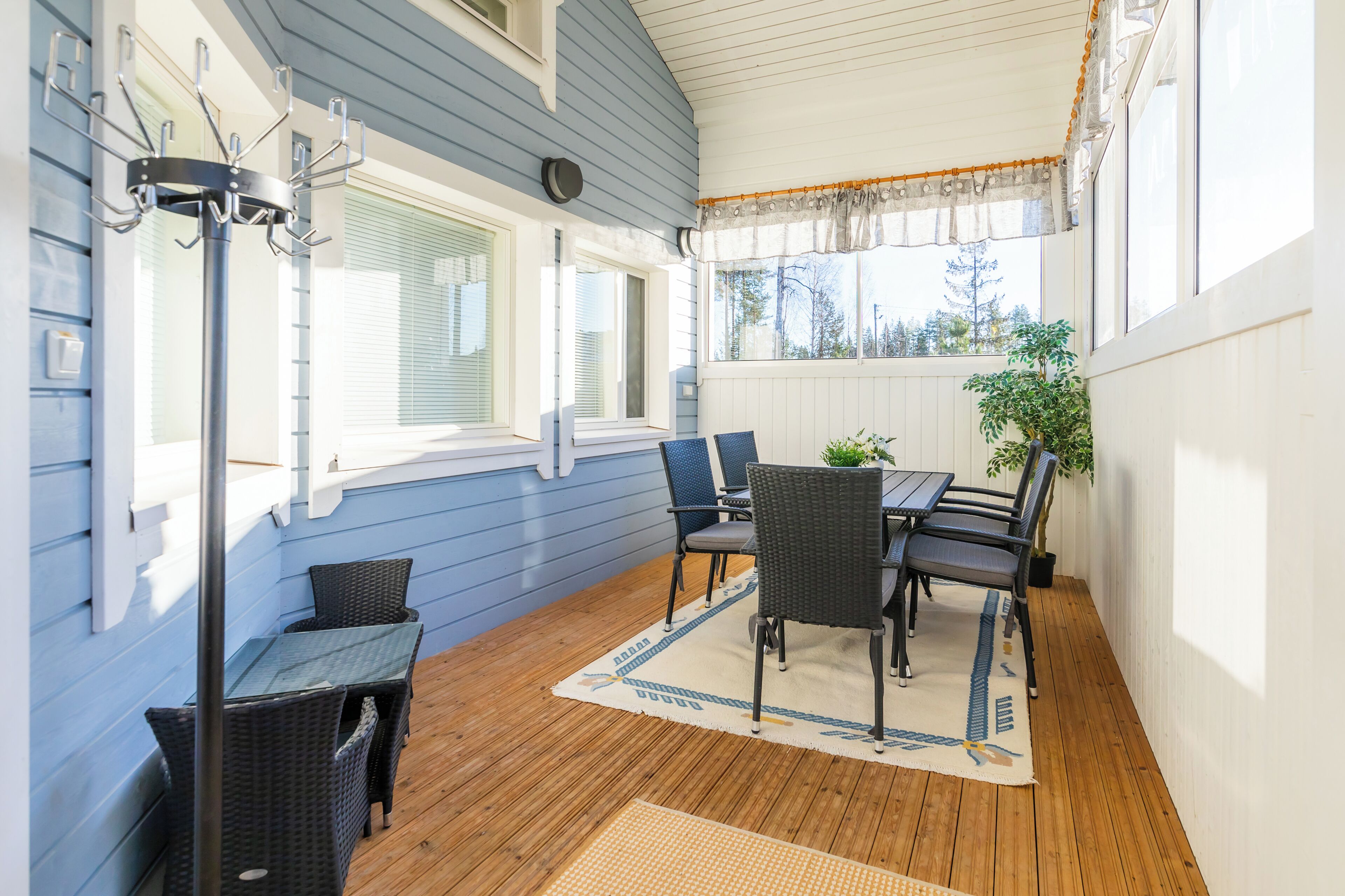 A covered patio with a wooden deck, a table with chairs, and a potted plant.