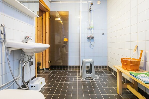 A bathroom with a sink, shower, and a wooden bench with a basket. - Lossisaari (Keitele)