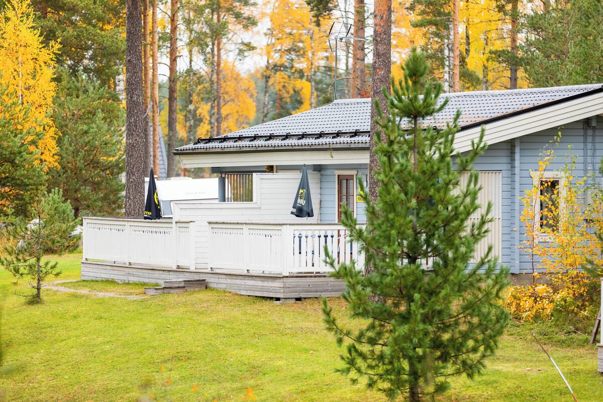 A small, single-story cabin with a porch, surrounded by trees with yellow leaves.