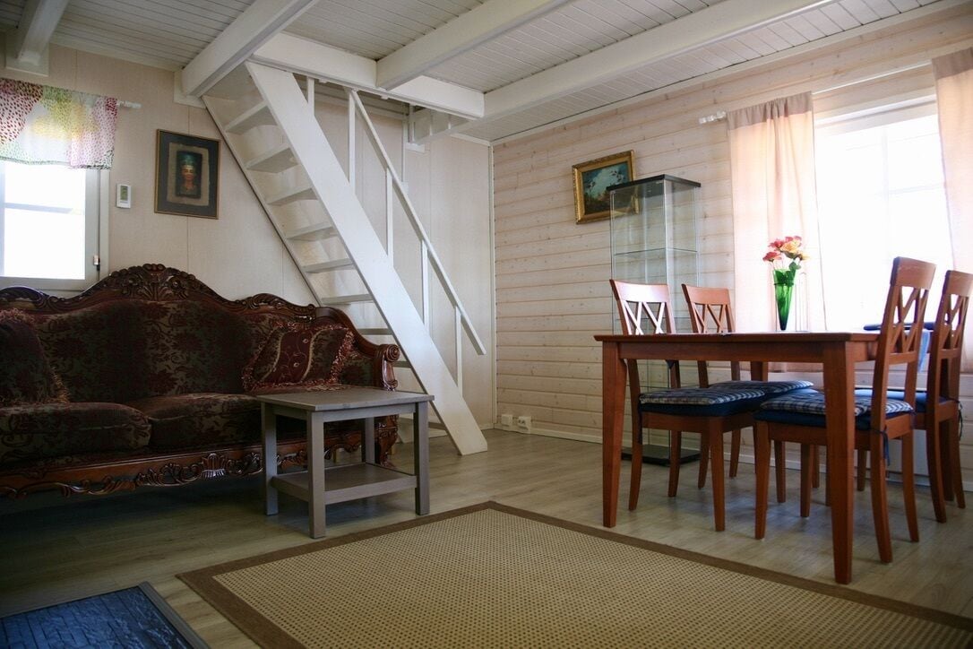 A living room with a staircase, a dining area with wooden chairs and a table, and a sofa.