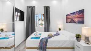 Una habitación de hotel moderna con una cama grande, televisor, un cuadro y una ventana con cortinas.