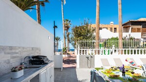 Un patio con una parrilla, mesa, sillas y vista al mar.