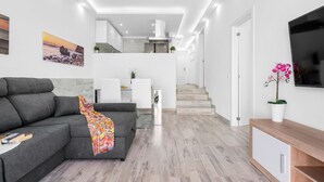 Una sala moderna con un sofá gris, una manta de colores y un televisor de pantalla plana sobre un mueble de madera.
