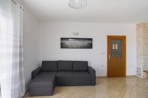 A living room with a sectional sofa, a door, a stone wall, and a picture on the wall. - Secluded Pool Villa Sofija Near Zadar (Škabrnja)