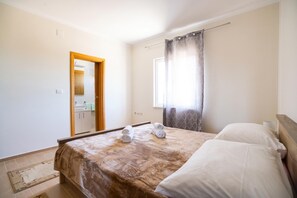 A hotel room with a bed, a bathroom visible through an open door, and a window with curtains.