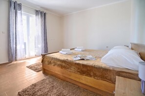 A hotel room with a wooden bed, a window with curtains, a wooden floor, and a small rug. - Secluded Pool Villa Sofija Near Zadar (Škabrnja)
