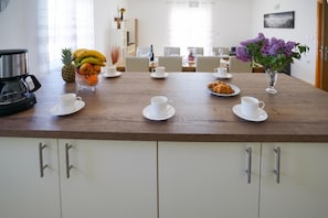 A breakfast setting with a wooden table, white cups, a fruit bowl, and a vase with flowers. - Secluded Pool Villa Sofija Near Zadar (Škabrnja)