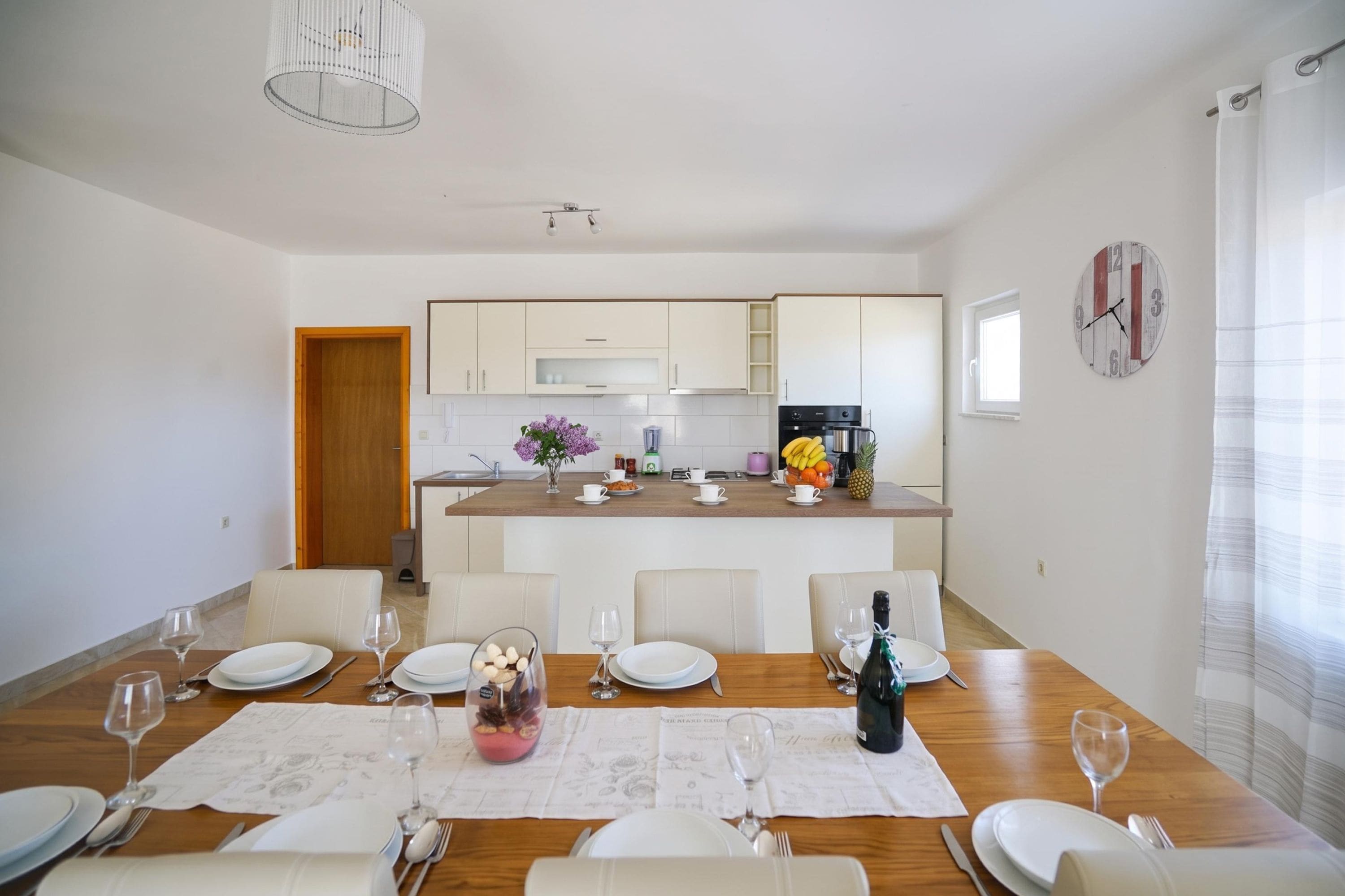 A modern kitchen with white cabinets, a wooden countertop, and a dining area with a table set for four.