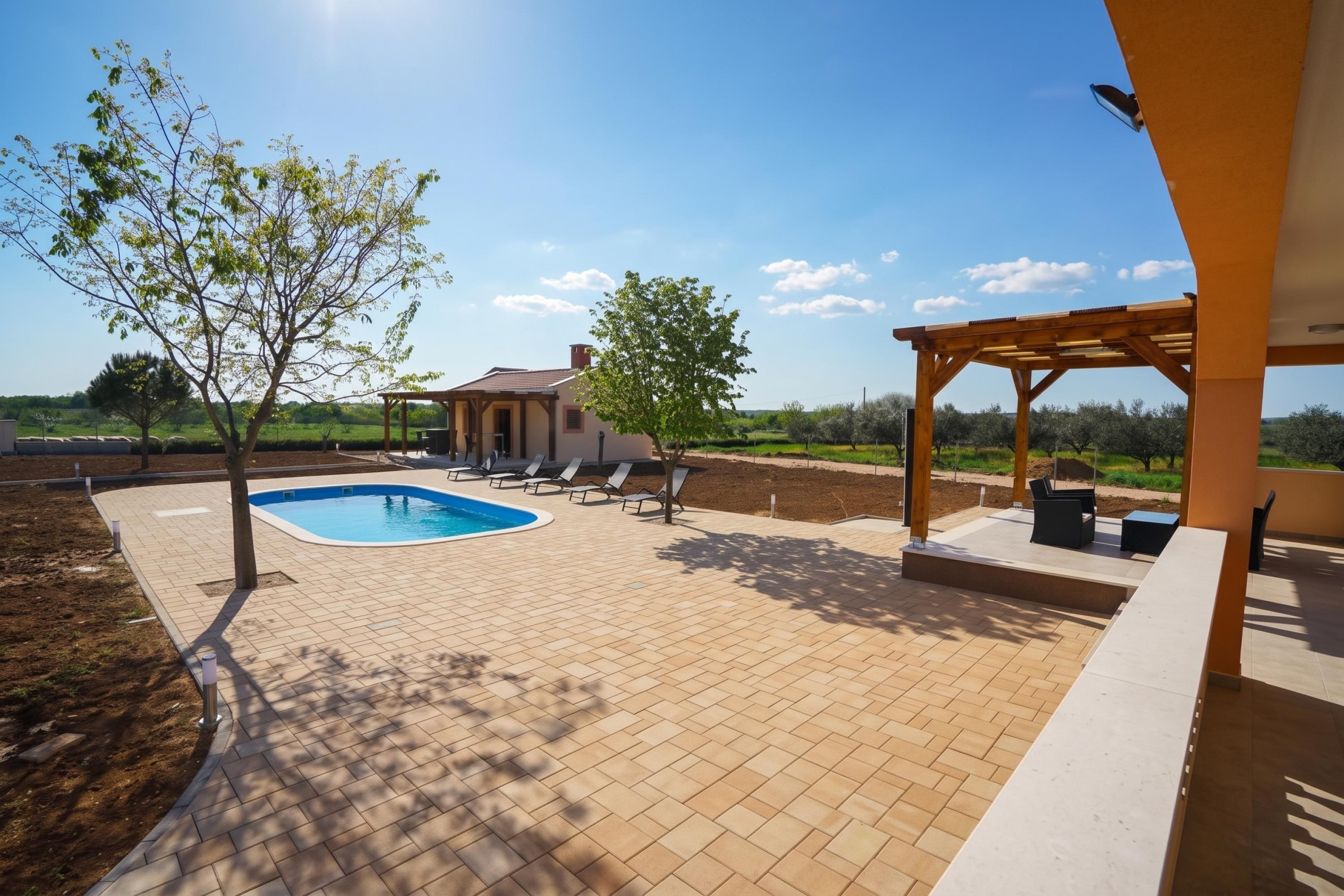 Ein Pool mit einer Pergola und Liegestühlen, umgeben von einem angelegten Garten und Blick auf die Landschaft.