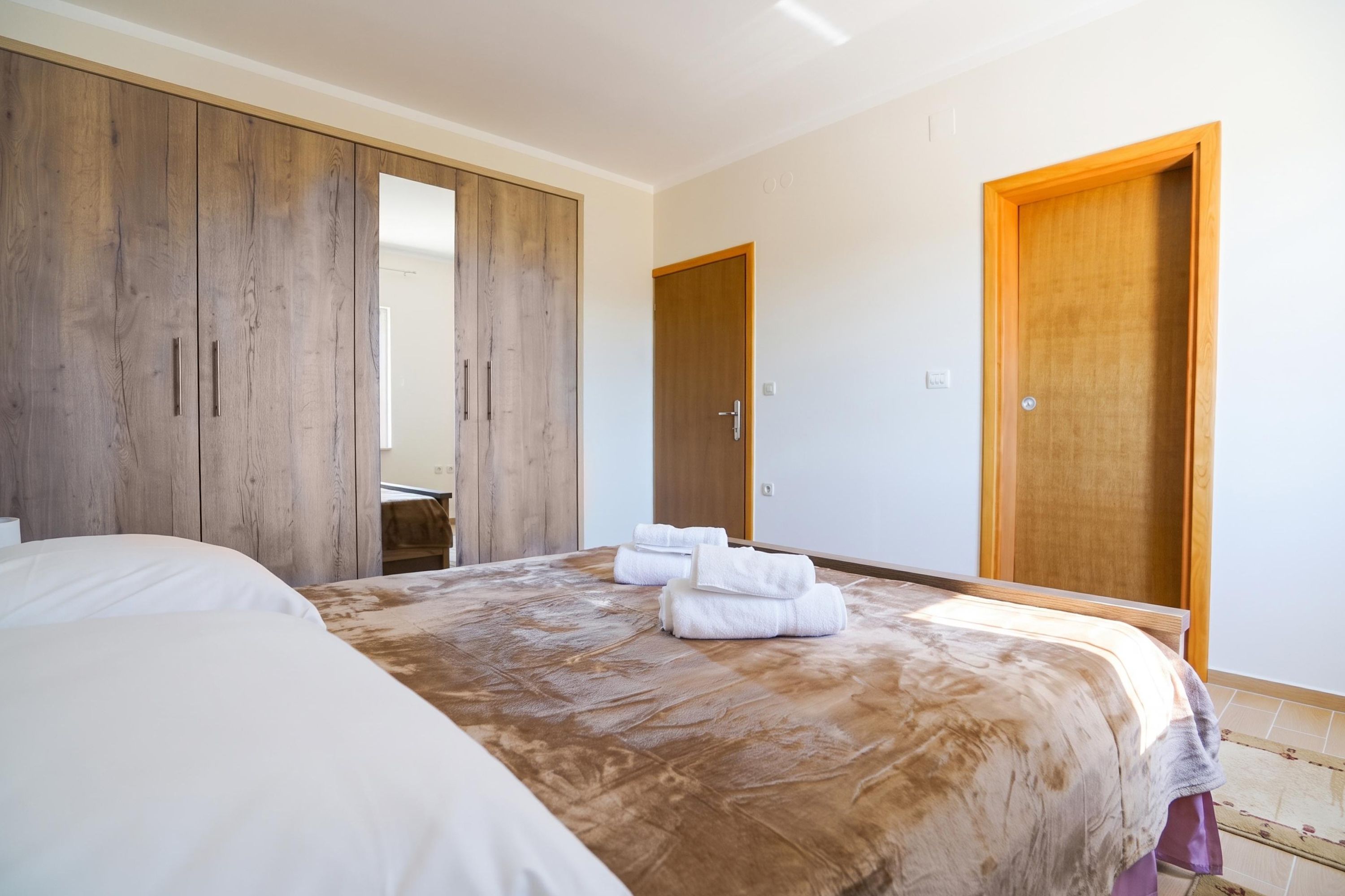 A bedroom with a large bed, wooden wardrobe, and a door.