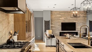 A modern kitchen with a gas stove, wooden cabinets, a built-in oven, a large island with a sink, and a stone backsplash. - Stunning Luxury Home Thunder Mtn Views + Hot Tub! (Sedona)
