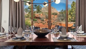 A dining table set with plates, bowls, and glasses, with a large window offering a view of a desert landscape. - Stunning Luxury Home Thunder Mtn Views + Hot Tub! (Sedona)