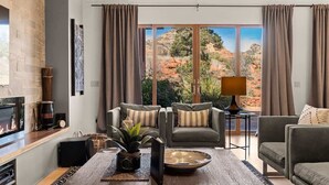 A living room with a fireplace, two sofas, a coffee table, and a view of red rock formations. - Stunning Luxury Home Thunder Mtn Views + Hot Tub! (Sedona)