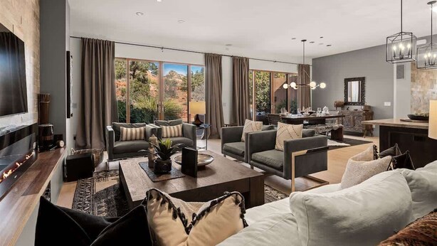 A spacious living area with a fireplace, comfortable seating, and large windows offering a view of the outdoors. - Stunning Luxury Home Thunder Mtn Views + Hot Tub! (Sedona)
