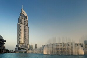 A tall, modern skyscraper with a unique curved top, surrounded by a body of water with a fountain display. - Amazing Stay & Burjview at The Address Dubai Mall (Dubai)