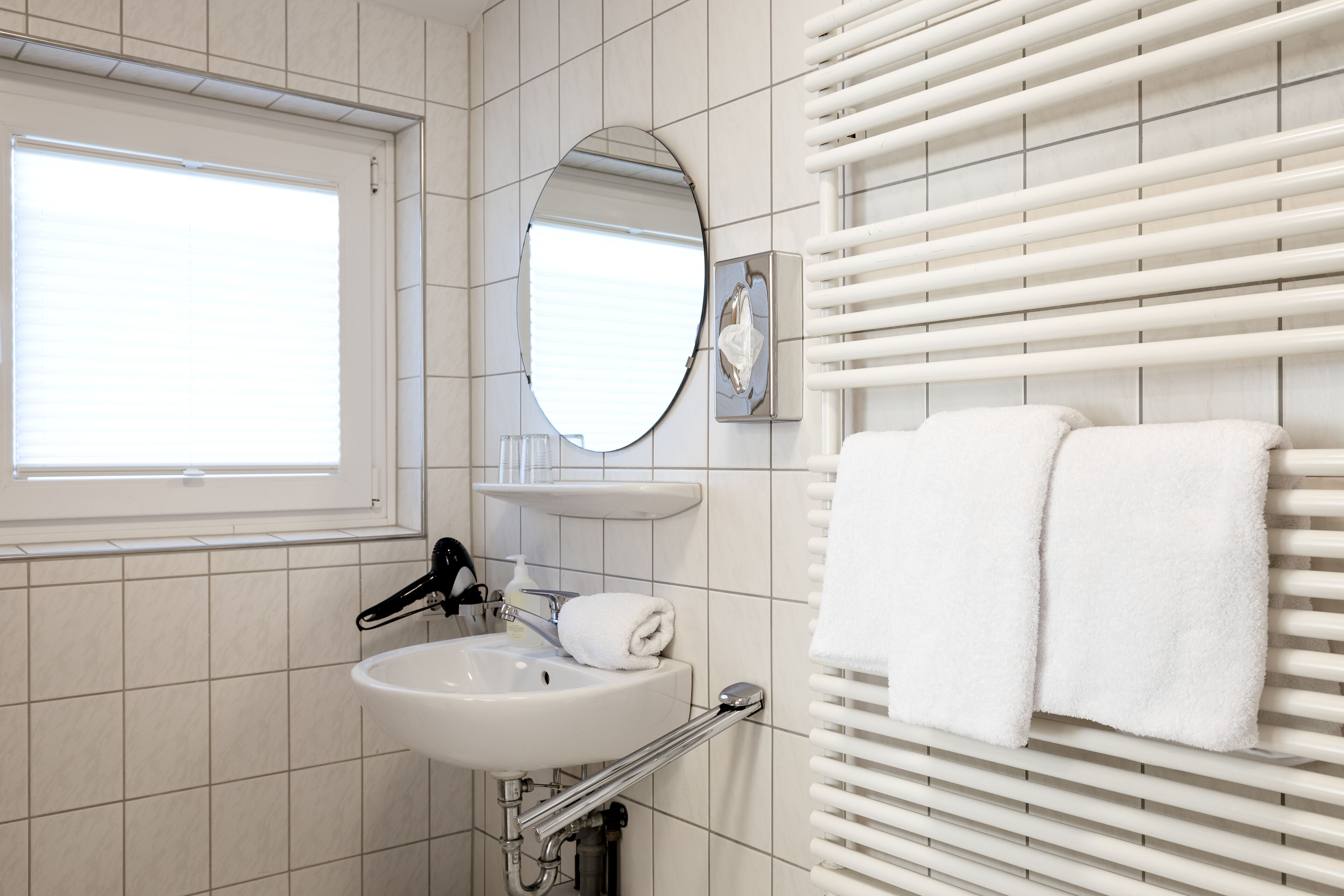 Un baño con lavamanos blanco, un espejo, toallero y ventana.