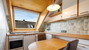 A compact kitchen with a dining area, a window, and a tiled backsplash. - Hummerklippen Apartments (Helgoland)
