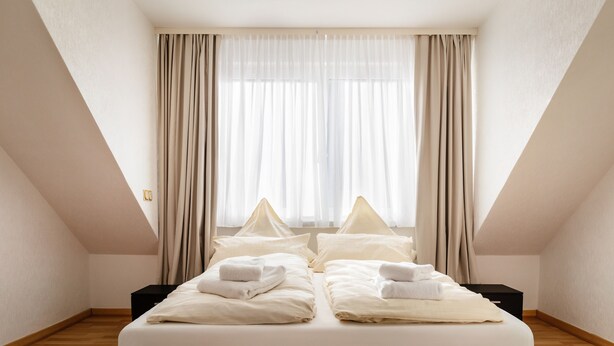 A hotel room with a bed, two nightstands, a window with curtains, and a wooden floor. - Hummerklippen Apartments (Helgoland)