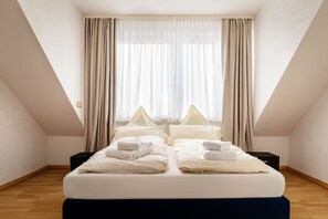 Habitación de hotel con cama, dos mesitas de noche, ventana con cortinas y suelo de madera.