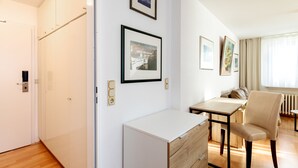 A modern hotel room with a wooden floor, a desk with a chair, a radiator, and framed pictures on the wall. - Hummerklippen Apartments (Helgoland)