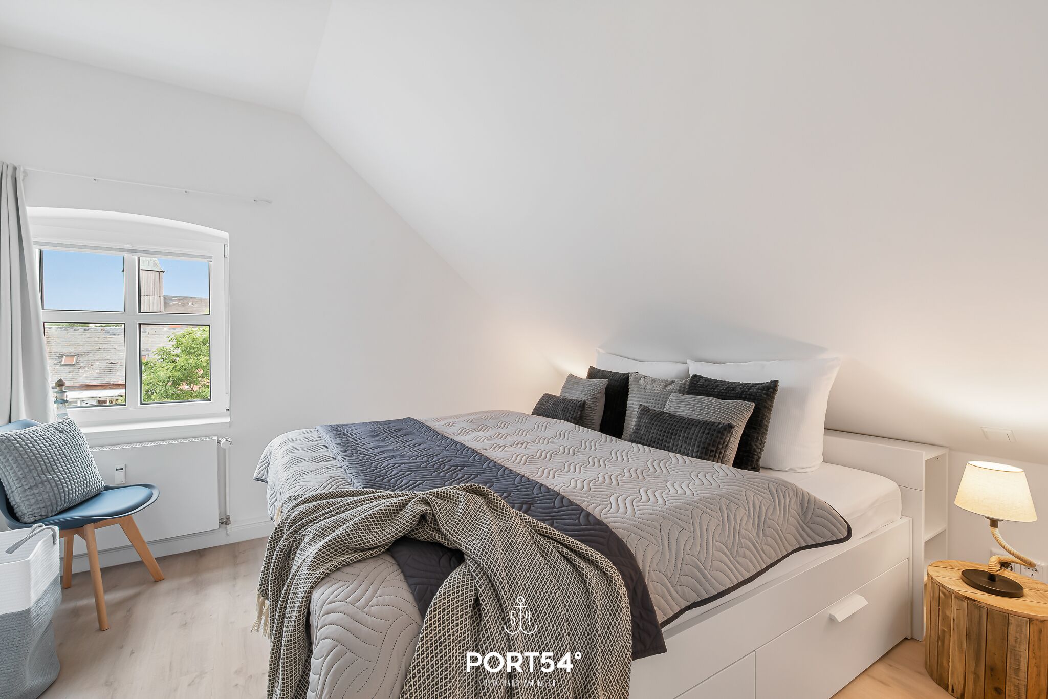 Une chambre à coucher avec un grand lit, une chaise, une table de chevet avec une lampe et une fenêtre avec des rideaux.
